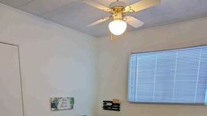 A bedroom with a bed, a ceiling fan, a window with blinds, a small shelf, and a door. - Oceanfront Cottage (Charlo)