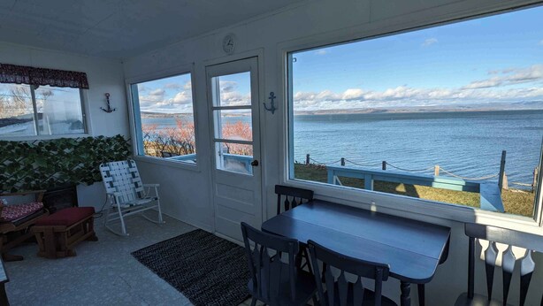 A room with a view of a lake, a dining table, a rocking chair, and a small rug. - Oceanfront Cottage (Charlo)