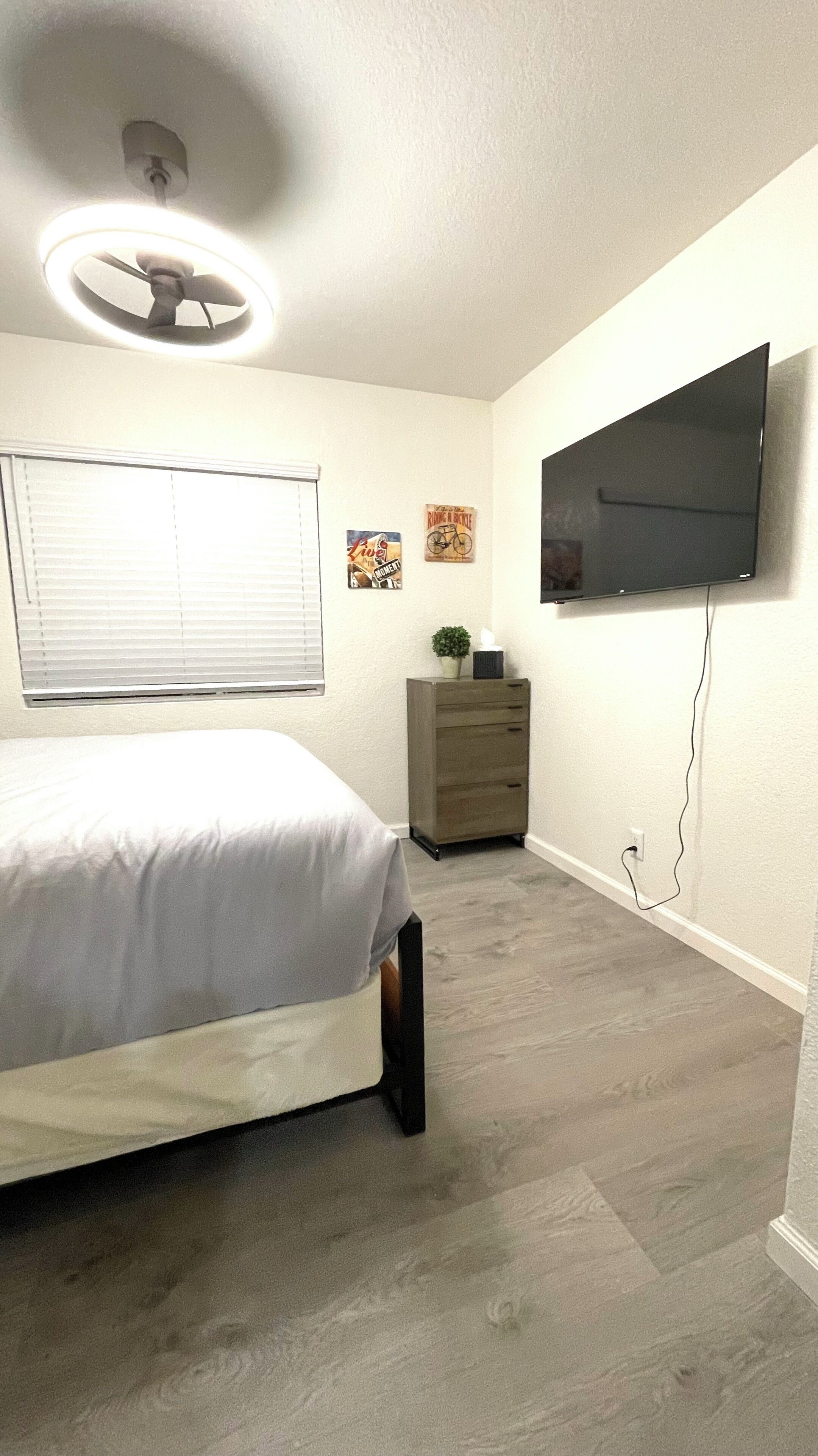 Une chambre à coucher comprenant un lit, une commode, un téléviseur fixé au mur et un ventilateur de plafond.