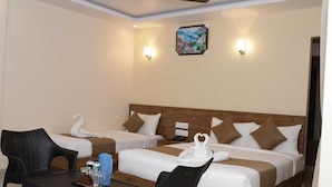 A hotel room with two beds, a dining table with chairs, and a ceiling fan.