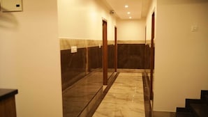 A hotel corridor with marble flooring, wooden doors, and a glass partition.