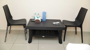 A small, dark-colored table with two chairs, a remote control, a tissue box, and two bottles on it.