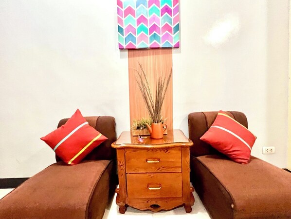 A small, cozy room with two brown sofas, a wooden nightstand with drawers, and a colorful chevron-patterned wall hanging.