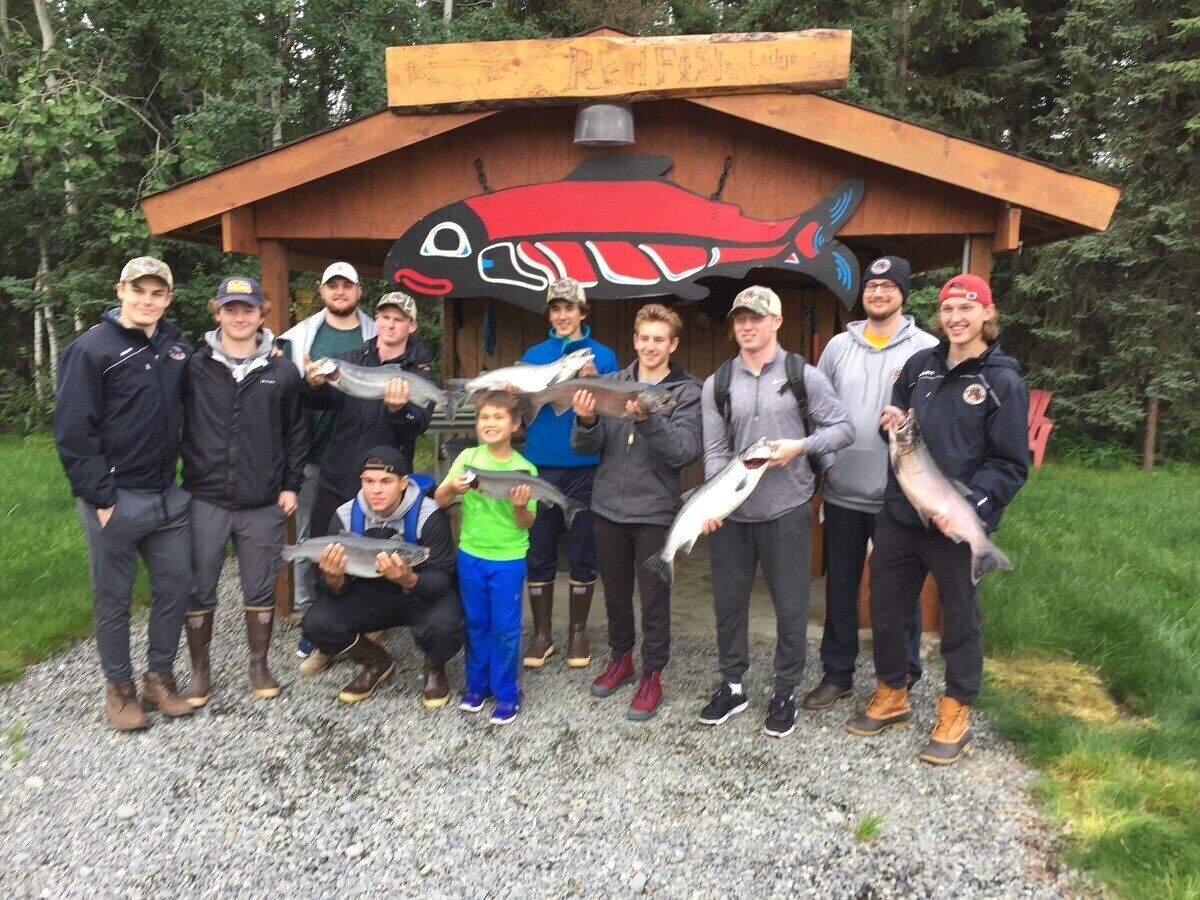 A group of people posing in front of a wooden structure with a fish mural.