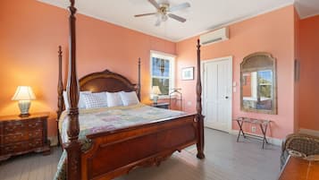 A four-poster bed with a wooden headboard, a ceiling fan, and a large window with a view of the outdoors.