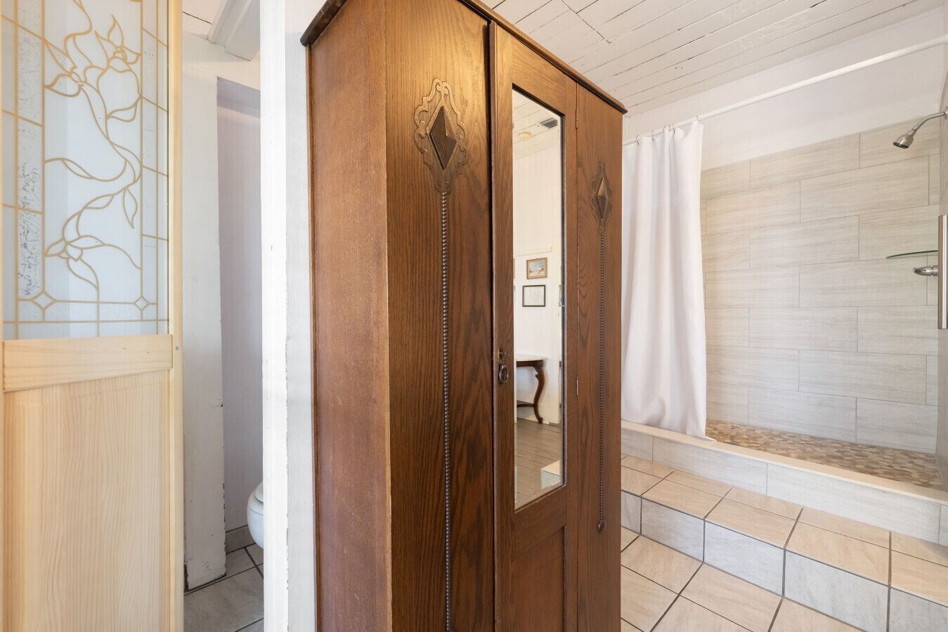 Een houten garderobe met spiegel, een douche met gordijn, en betegelde vloer.