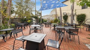 An outdoor patio with tables and chairs, surrounded by palm trees and a building with a balcony. - The Historic Island Hotel of Cedar Key (Cedar Key)