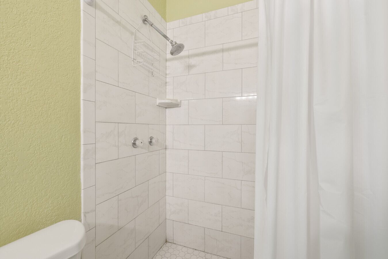A bathroom with white tiles, a shower, and a toilet.