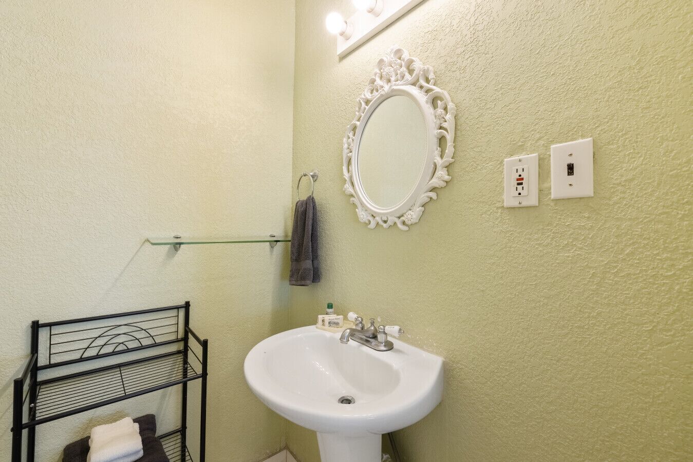 Un baño con un lavamanos blanco, un espejo y un perchero para toallas.