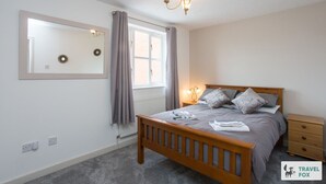 A bedroom with a wooden bed, a nightstand, a mirror, and a window with curtains. - Sarah`s House: BBQ Parking 10mins To Alton Towers (Alton Towers & Staffordshire Villages)