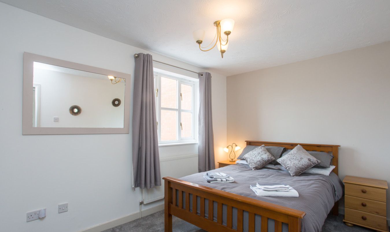 A bedroom with a wooden bed, a nightstand, a mirror, and a window with curtains.