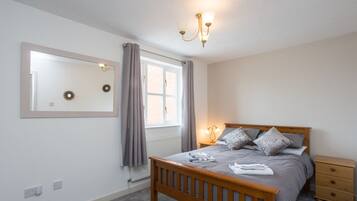 A bedroom with a wooden bed, a nightstand, a mirror, and a window with curtains.