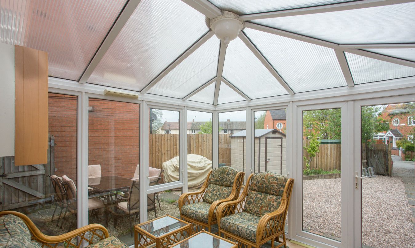 A conservatory with wicker furniture, a glass table, and a view of a backyard.