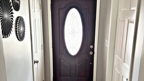 Un pasillo con una puerta de madera oscura, paredes blancas y suelo de madera.