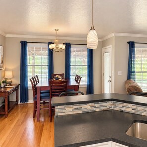 A kitchen with a dark countertop, a dining area with wooden chairs, and a chandelier.