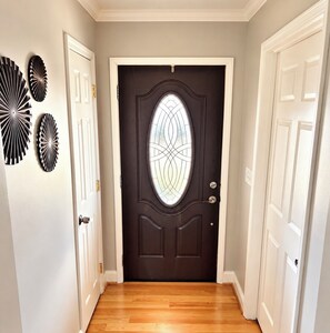Un couloir avec une porte en bois sombre ornée d’un panneau de verre décoratif, flanquée de portes blanches et de plaques décoratives fixées au mur.