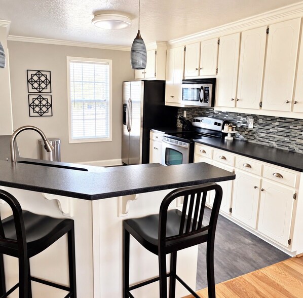 A kitchen with a central island, white cabinets, a black countertop, and a stainless steel refrigerator.