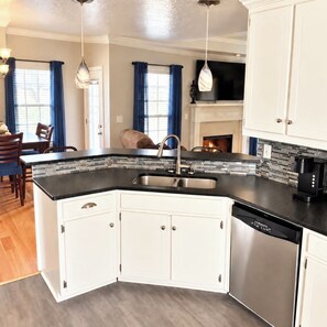 A kitchen with white cabinets, a black countertop, a stainless steel dishwasher, and a hanging light fixture.