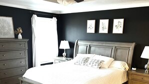 Un dormitorio con una cama grande, un aparador, una mesita de noche y una lámpara de pared.