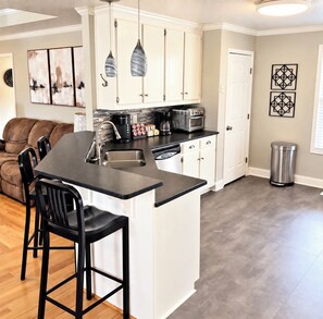 A kitchen with a central island, white cabinets, a coffee maker, and a trash can.