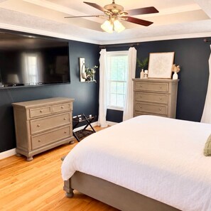 A bedroom with a bed, a dresser, a TV, and a ceiling fan.