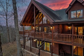 A log cabin with a balcony, large windows, and a view of the surrounding forest.