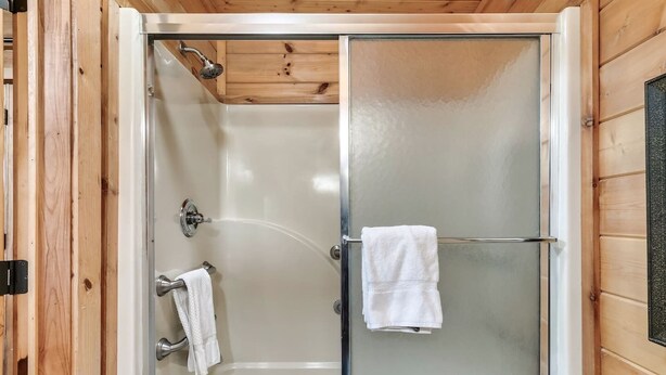 Un box de ducha con puerta de cristal, una toalla blanca en la pared y revestimiento de madera.