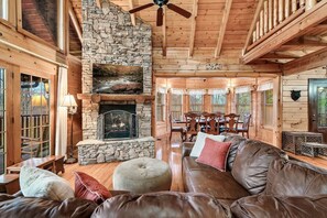 A log cabin interior with a stone fireplace, wooden furniture, and a dining area. - GatlinByrd Lodge! Indoor Pool/Hot Tub/Pet Friendly (Sevierville)