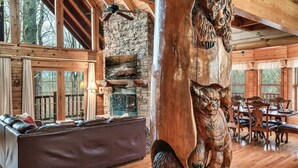 Interior de una cabaña de troncos con chimenea de piedra, mobiliario de madera y una gran escultura de madera.
