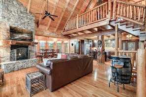 A spacious cabin interior with a stone fireplace, wooden floors, a leather sofa, and a dining area. - GatlinByrd Lodge! Indoor Pool/Hot Tub/Pet Friendly (Sevierville)