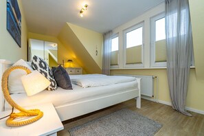 Ein Schlafzimmer mit Bett, Nachttisch, Lampe und einem Fenster mit Vorhängen.