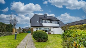 A two-story house with a paved driveway leading to the front door, surrounded by well-maintained hedges and a wooden fence. - Tom - 3-room vacation apartment on the 1st floor in Westerland with terrace. (Sylt)