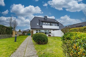 Ein zweistöckiges Haus mit gepflasterter Auffahrt zum Eingang, umgeben von gepflegten Hecken und einem Holzzaun.