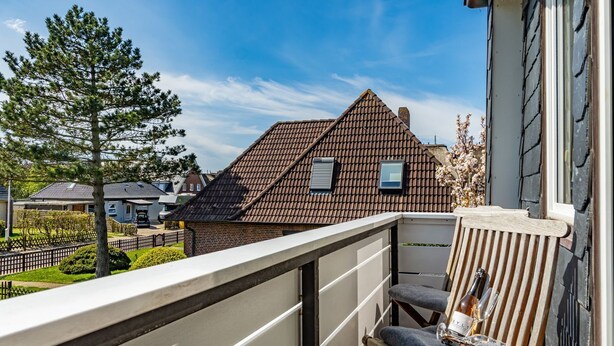 A balcony with a chair and a table, a tiled roof, and a view of neighboring houses. - Tom - 3-room vacation apartment on the 1st floor in Westerland with terrace. (Sylt)