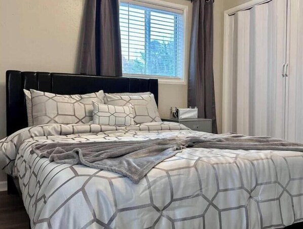 A neatly made bed with a geometric patterned duvet and pillows, a bedside table with a lamp, and a window with blinds.