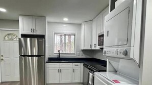 A compact kitchen with white cabinets, a stainless steel refrigerator, a built-in oven, and a washing machine. - Modern 2BR Stylish Retreat A Upstairs (Atlanta)