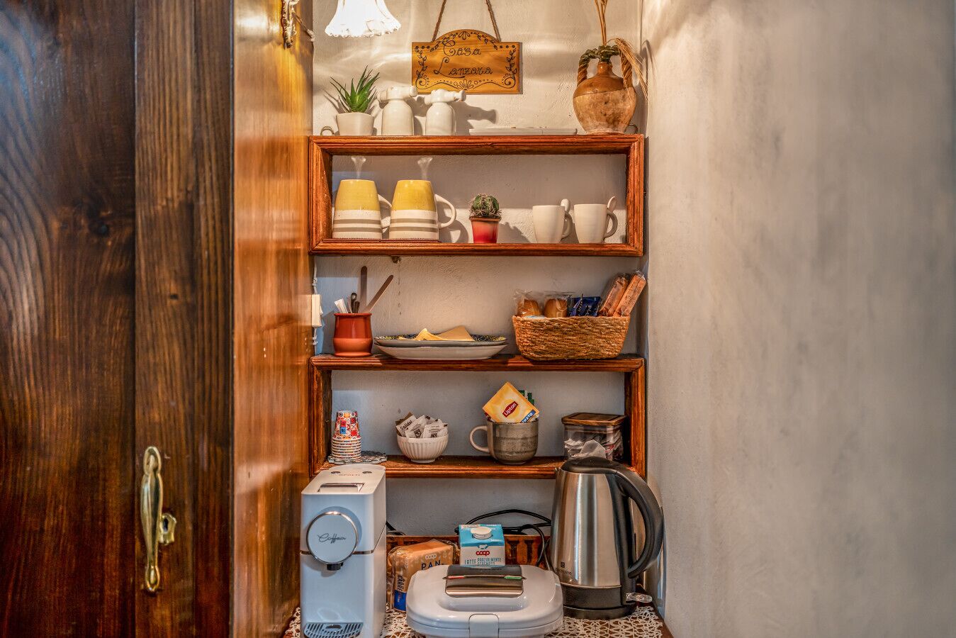A kitchen with wooden shelves, a coffee machine, a kettle, and various kitchen items.