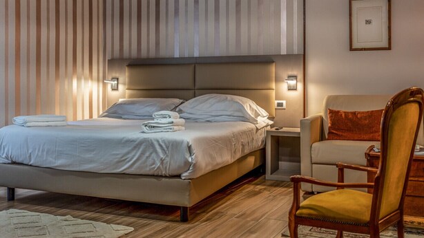 A hotel room with a bed, bedside tables, a chair, and a wall-mounted picture.