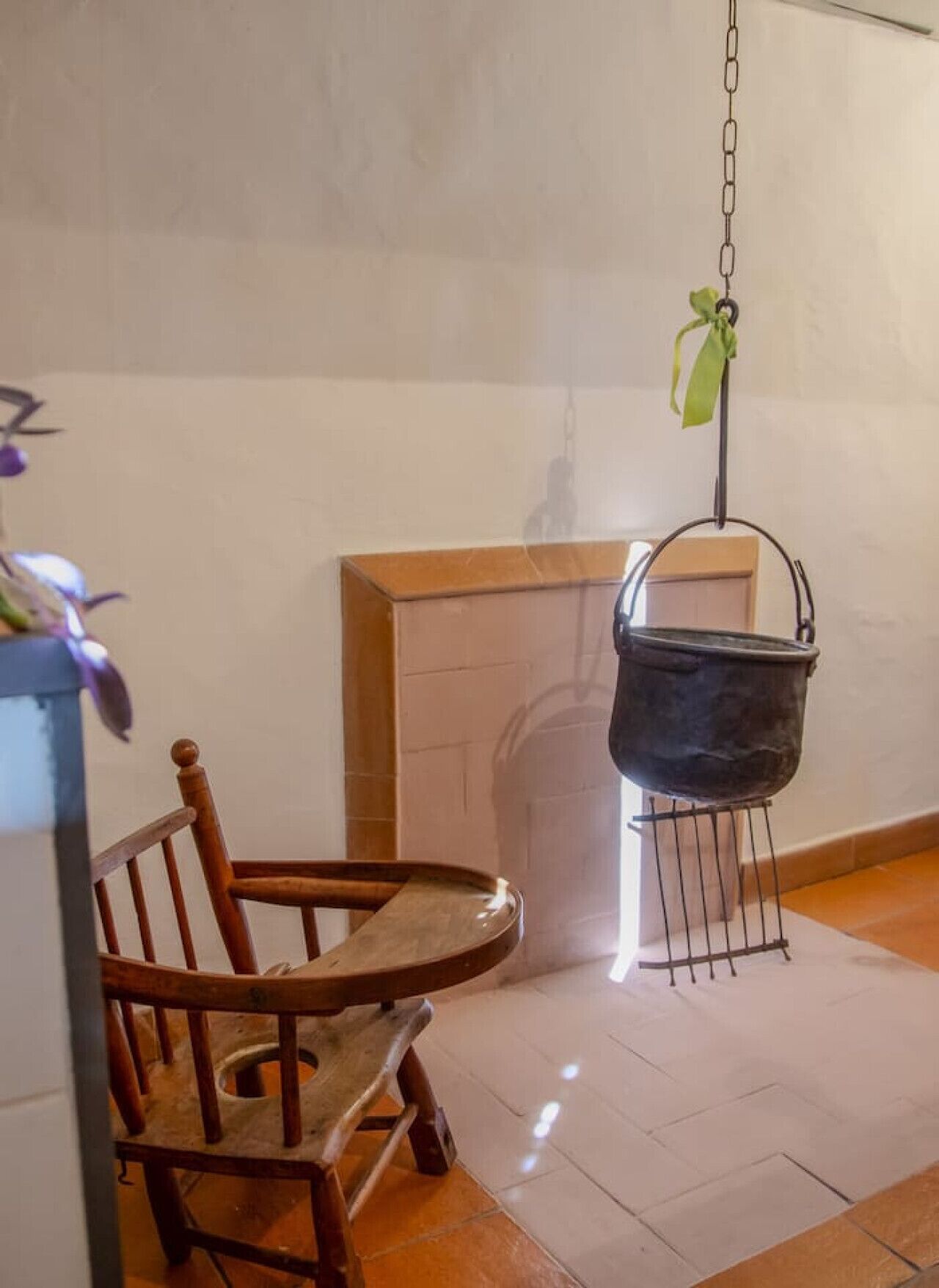 Una habitación rústica con una silla de madera, una chimenea y una olla colgante.