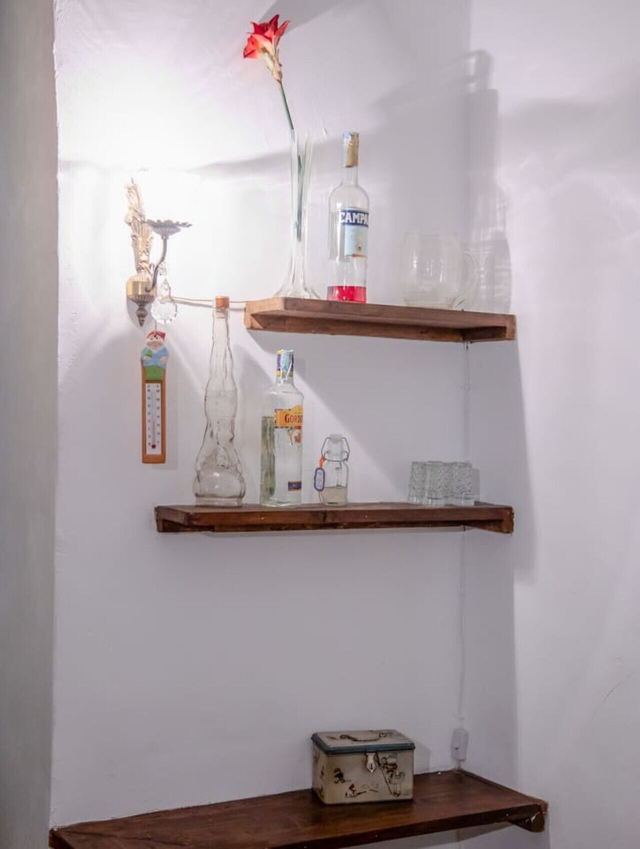 A wall-mounted shelf with various items including a thermometer, a bottle of alcohol, a glass jar, and a small box.
