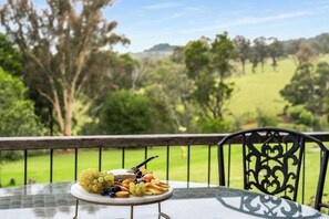 Una mesa con una bandeja de frutas en un balcón con vistas a un paisaje cubierto de hierba.
