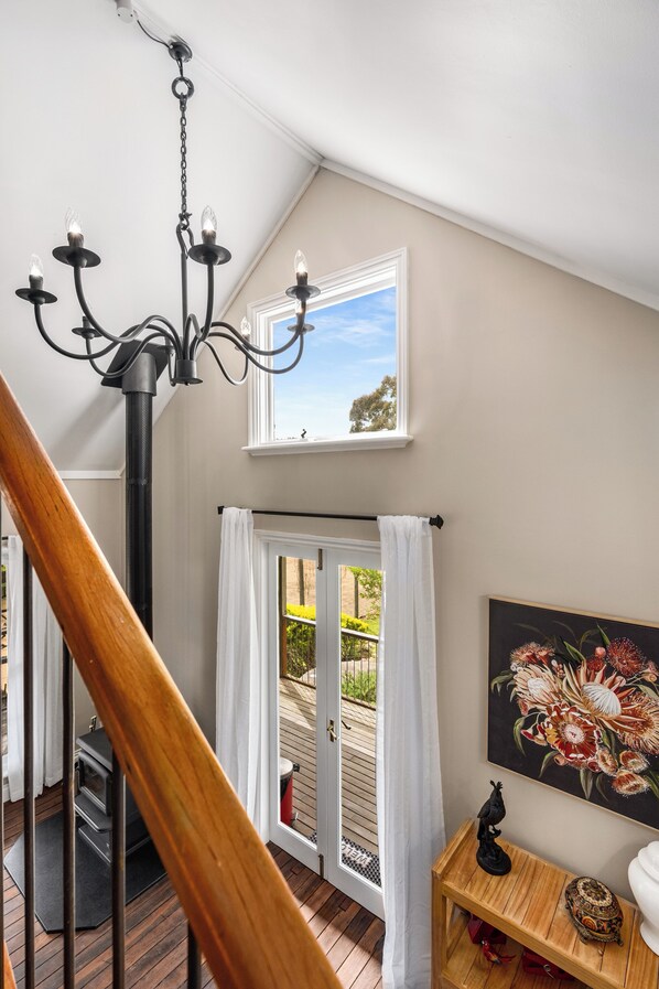 Una escalera conduce a un balcón con vistas a follaje, un candelabro y un cuadro de flores.