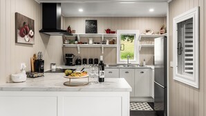 Una cocina moderna con armarios blancos, encimera de mármol y horno empotrado. Hay copas de vino, una botella y un frutero sobre la encimera.