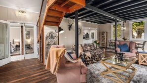 Amplia sala de estar con techo alto, vigas de madera, una escalera y un ventanal grande.