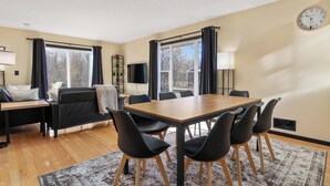 A modern living room with a wooden dining table, black chairs, a sofa, and a TV. - Zen Den Oasis: Retreat in Nature, 4-Bedroom Home on 10 Acres of Private Land (Cottage Grove)