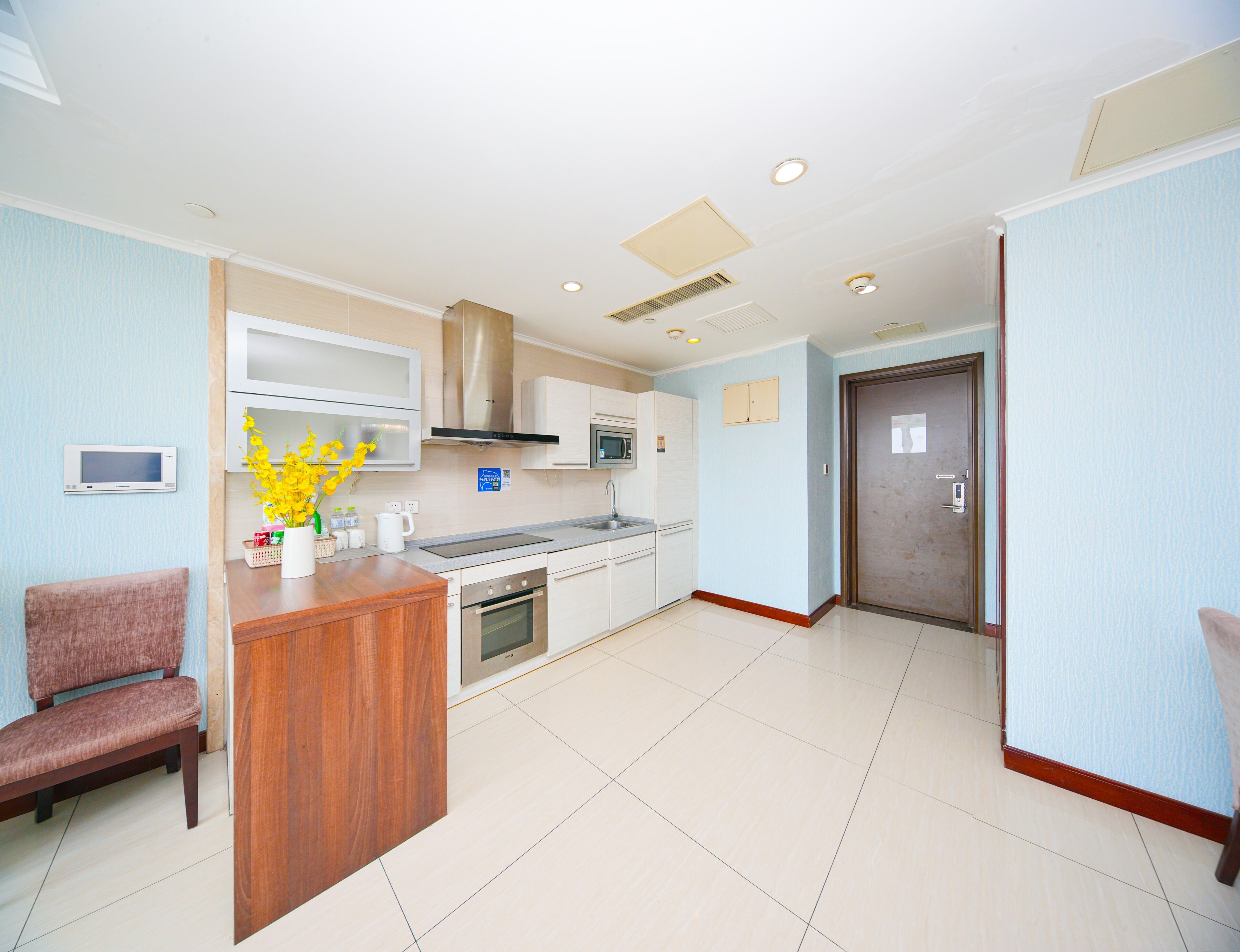 A modern kitchen with white cabinets, a microwave, and a stove. There is a wooden counter and a chair.