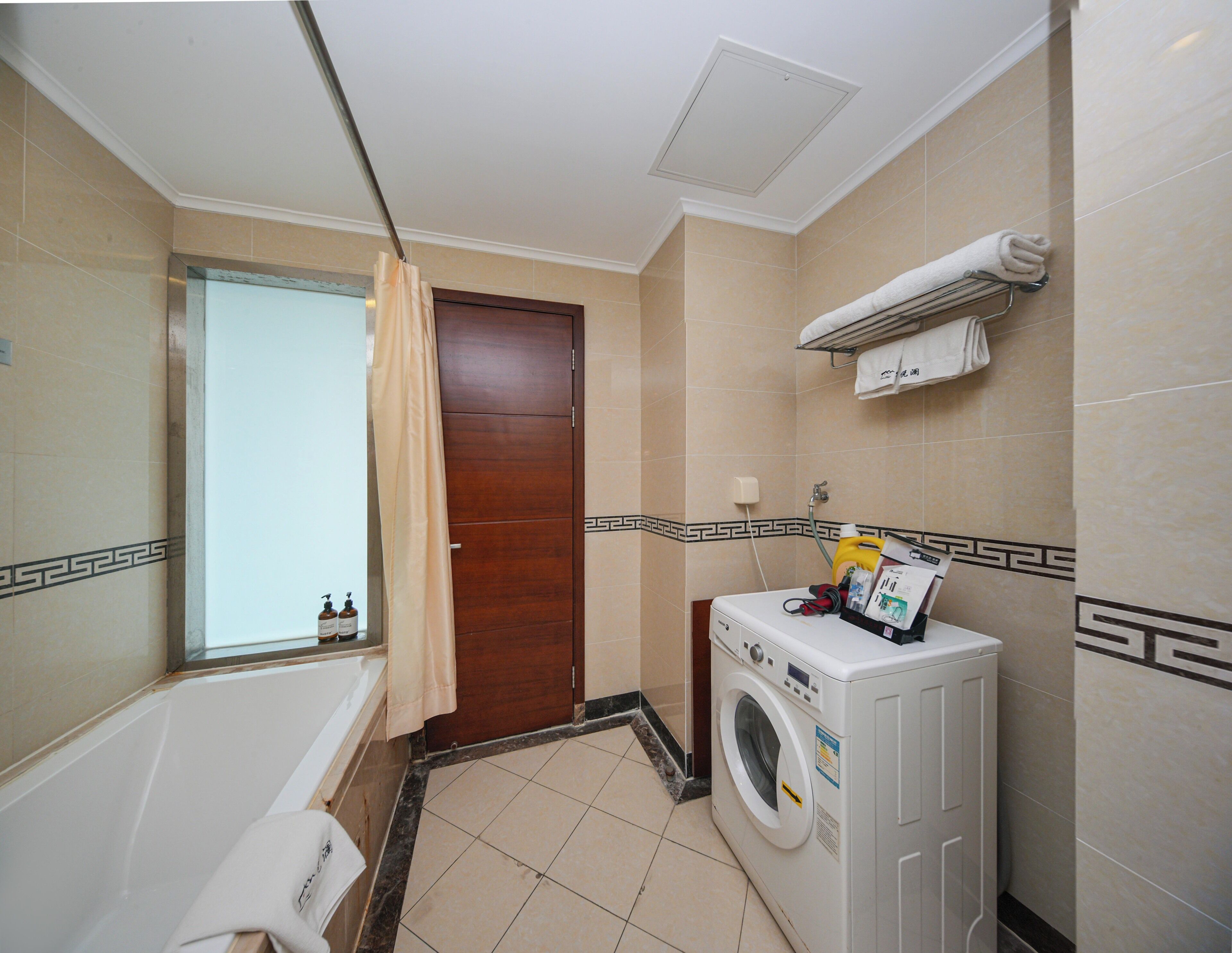 A compact bathroom with a bathtub, a shower, and a built-in washing machine.
