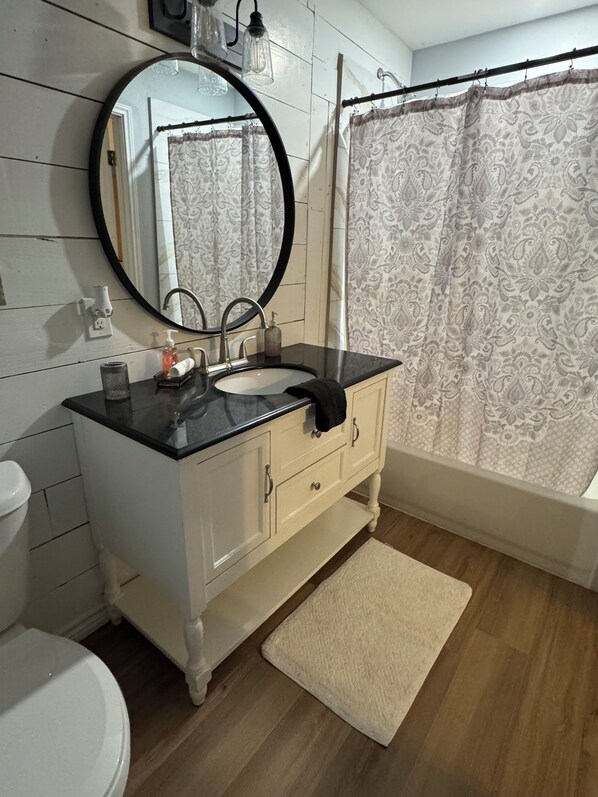 A bathroom with a round mirror, a sink, a toilet, and a shower curtain.