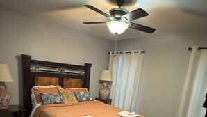 A bedroom with a bed, a ceiling fan, a nightstand, a lamp, and a window with curtains. - Gorgeous quiet and cozy 3 bedroom/ 2 bathroom home awaits you! (Uvalde)