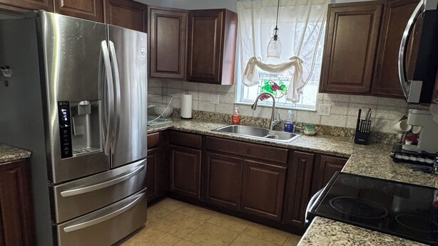 A kitchen with dark wooden cabinets, a stainless steel refrigerator, a granite countertop, and a black stove. - Gorgeous quiet and cozy 3 bedroom/ 2 bathroom home awaits you! (Uvalde)